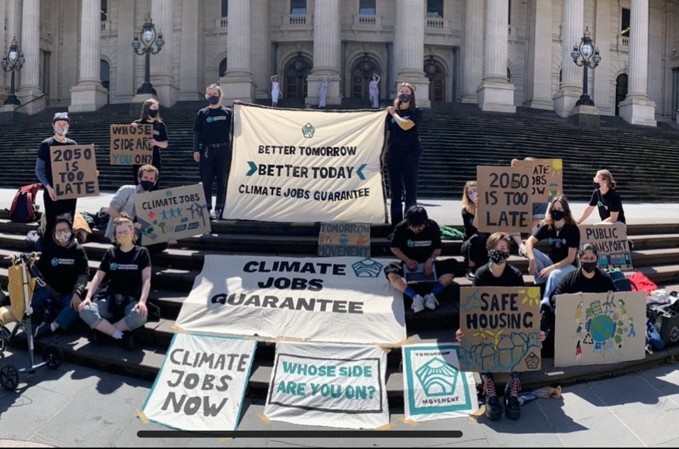 Group of young people on the steps of Victorian Parliament house holding white banners that say Climate jobs guarantee